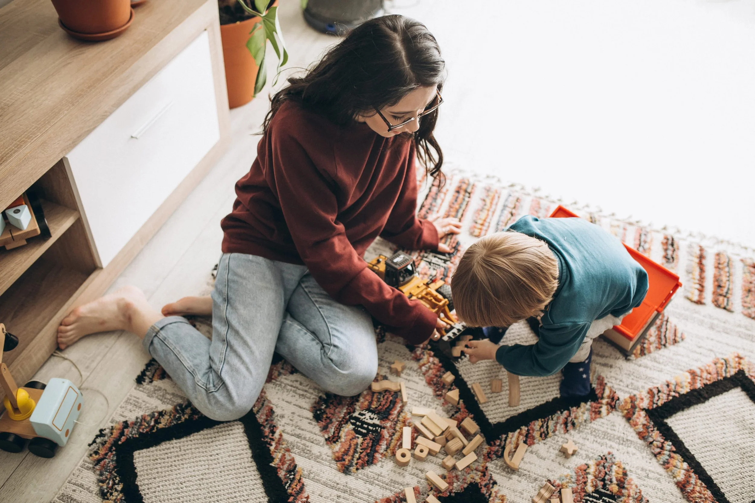 Nanny playing trucks with little boy on the floor