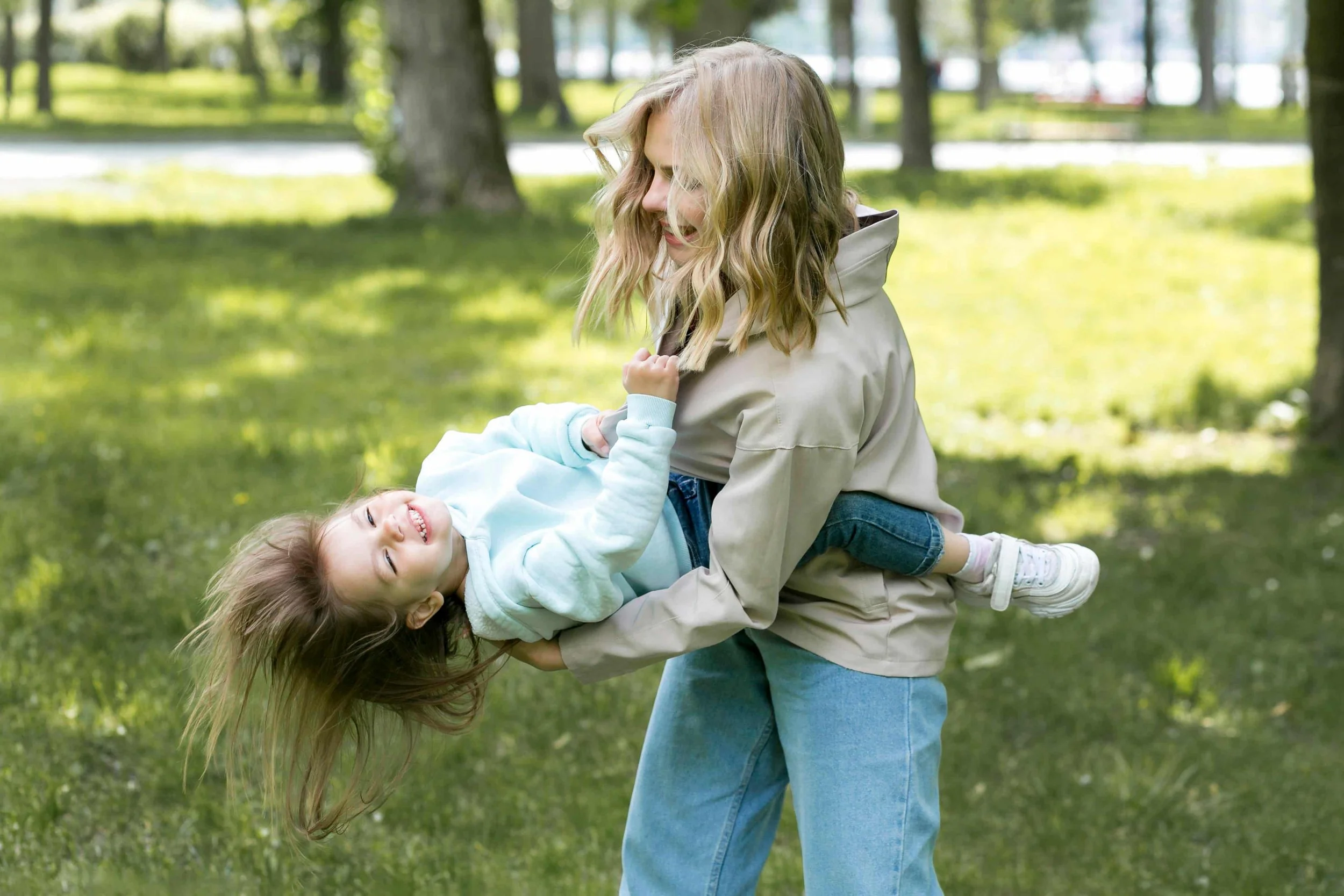Nanny holding little girl in the air outside at the park