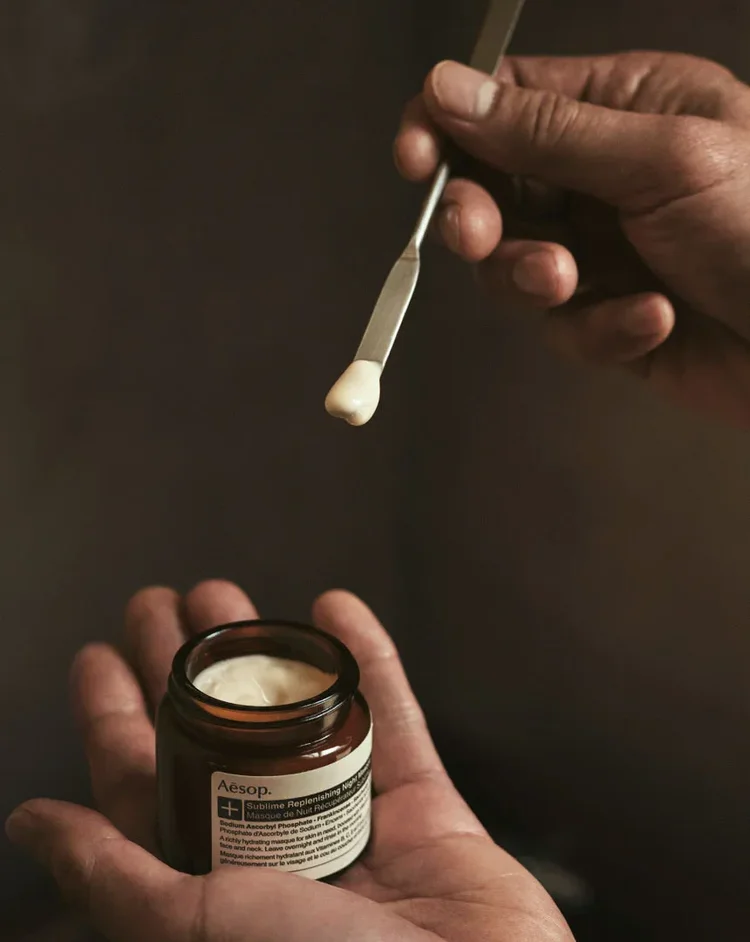 Aesop skincare jar held in the palm with a spatula