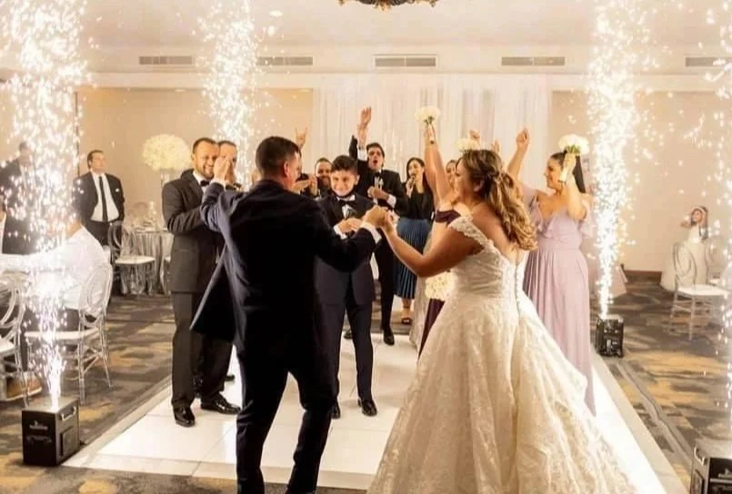 Wedding reception with bride and groom dancing surrounded by guests and indoor fireworks.