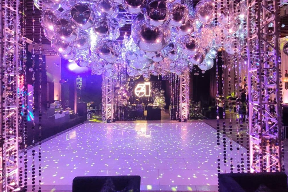 Elegant event space with a glossy dance floor, reflective ceiling decor, LED lighting, and decorative columns. Ambient purple and silver tones create a luxurious atmosphere.