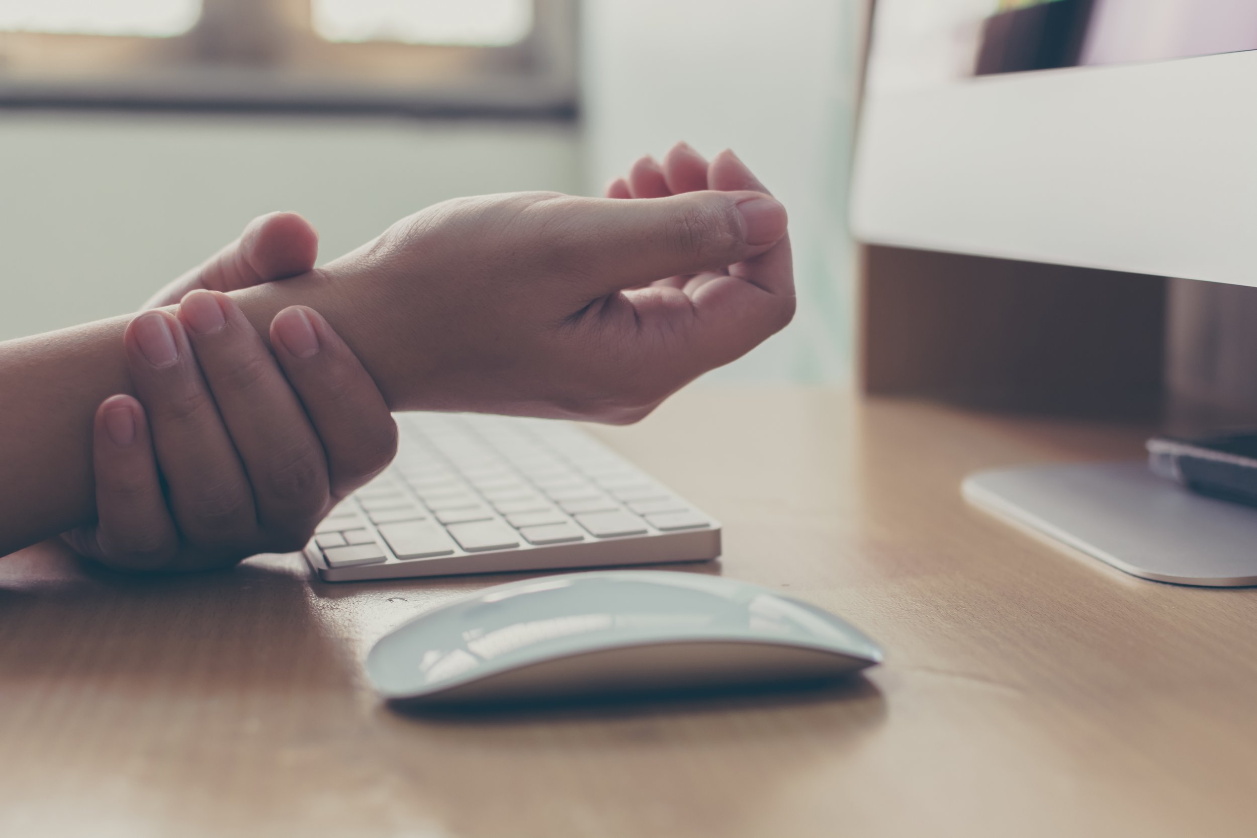 A person prevents a wrist injury using a splint or brace while working at a computer with a keyboard and mouse