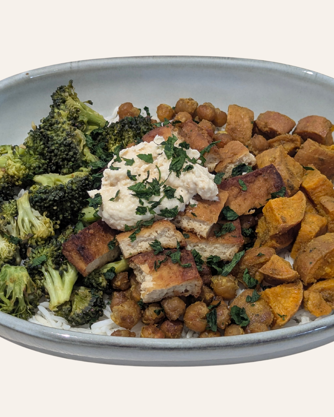 Grey ceramic bowl with broccoli, tofu, hummus, rice, chickpeas and sweet potato