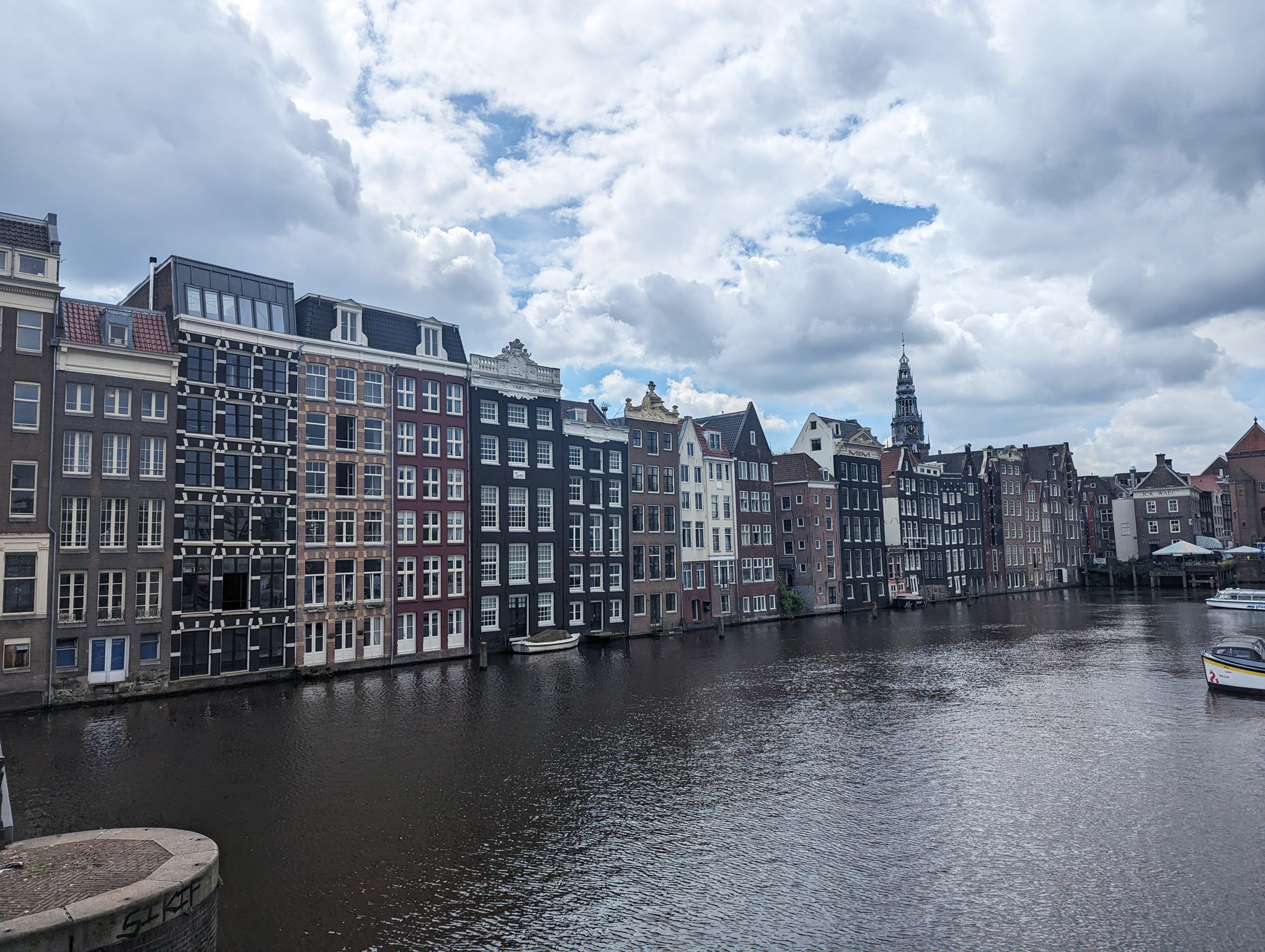 A row of buildings along the canal in Amsterdam, under a bright but cloudy sky.
