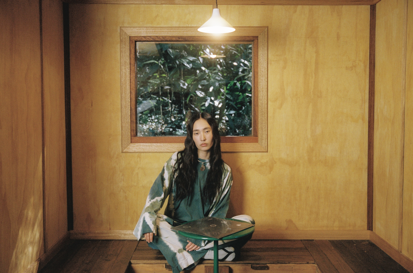 Woman sitting in cabin, showcasting tie dye clothing collection and choker necklace.