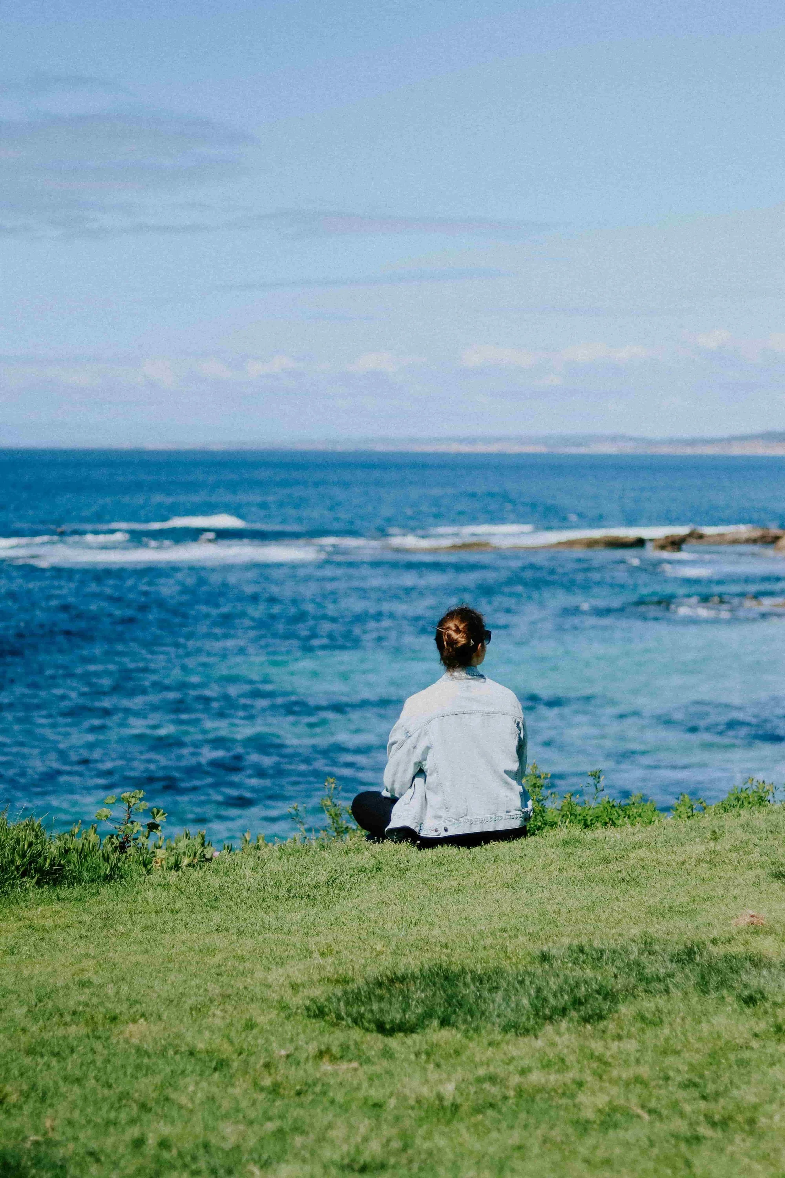 What It Means to Heal Trauma Through the Body -Woman sitting cross legged by the ocean