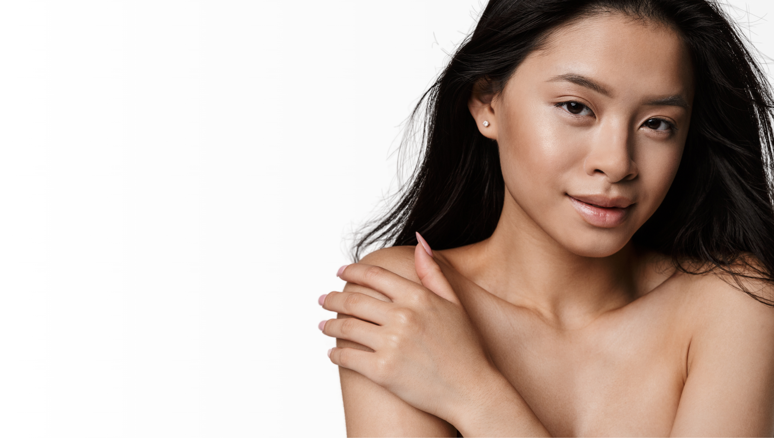 A young woman with long, dark hair, fair skin, and subtle makeup, posing with her hand on her shoulder against a plain white background.