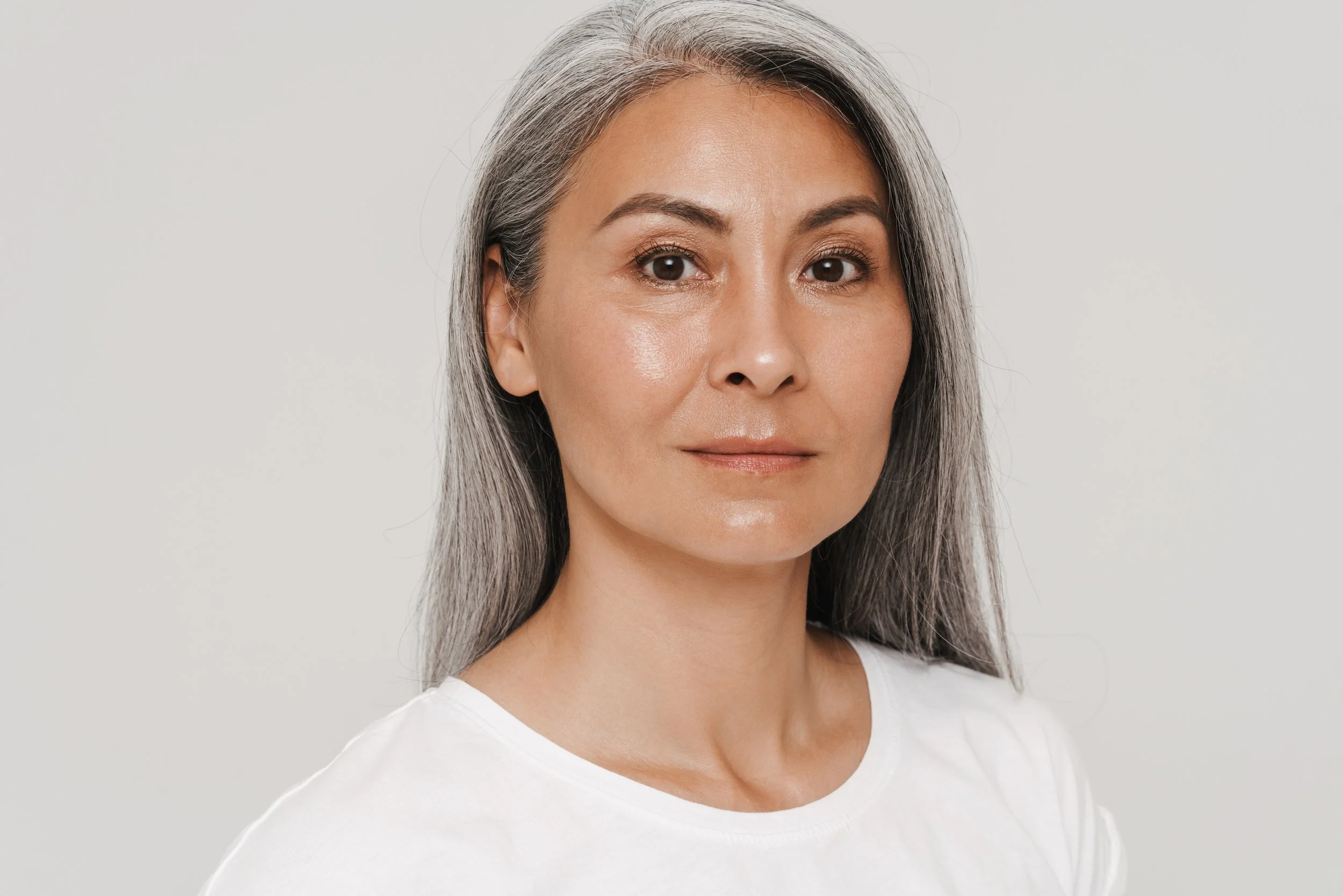 A portrait of a middle-aged woman with long gray hair, wearing a white top, against a plain light background.