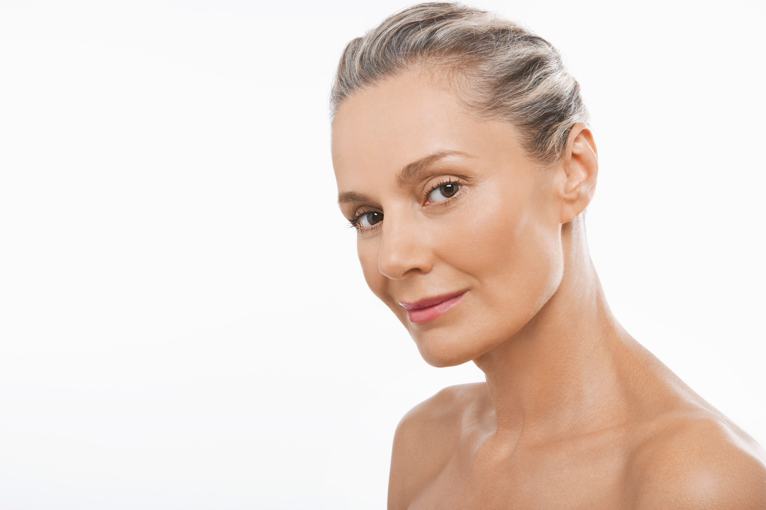 Close-up portrait of a smiling woman with flawless skin and short gray hair, looking directly at the camera against a plain white background.