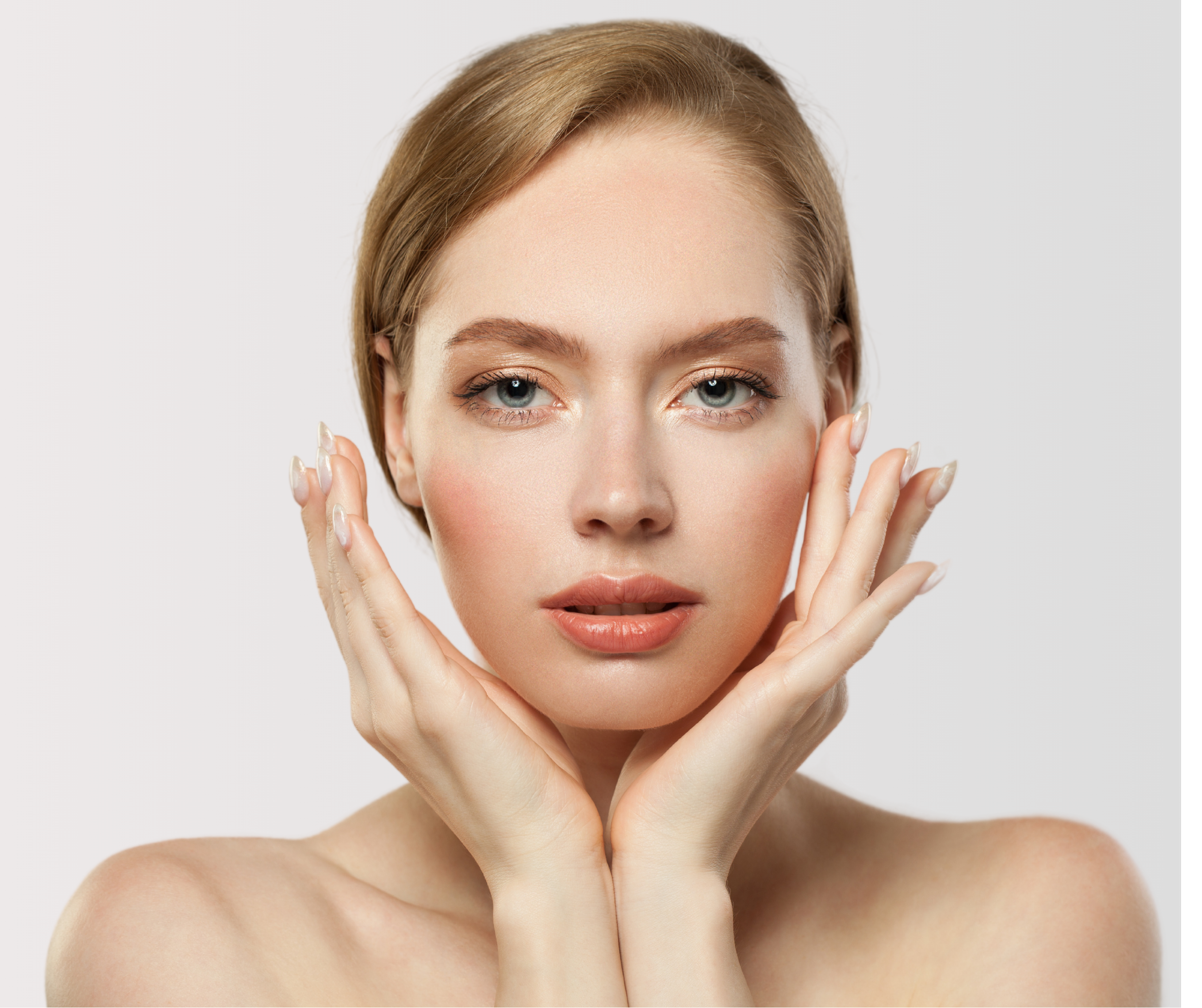 Close-up of a young woman with fair skin, blue eyes, and light brown hair, gently holding her face with both hands against a plain white background.