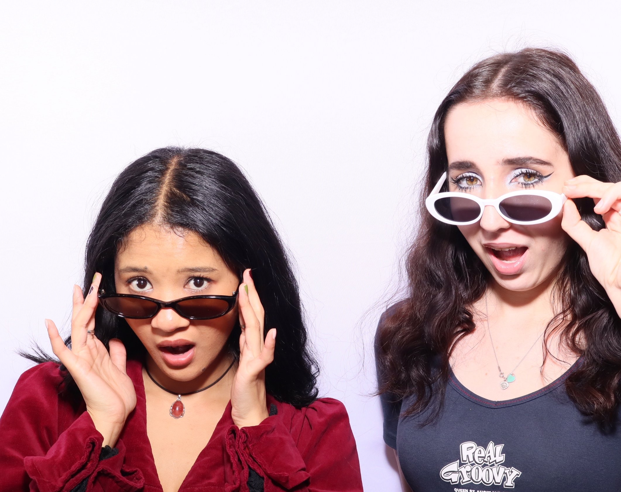 Two women posing with surprised expressions wearing sunglasses against a plain white background. This is taken at Record Store Day 2025 at Real Groovy Records Auckland with a photobooth by Royale Booths photobooth hire in Auckland