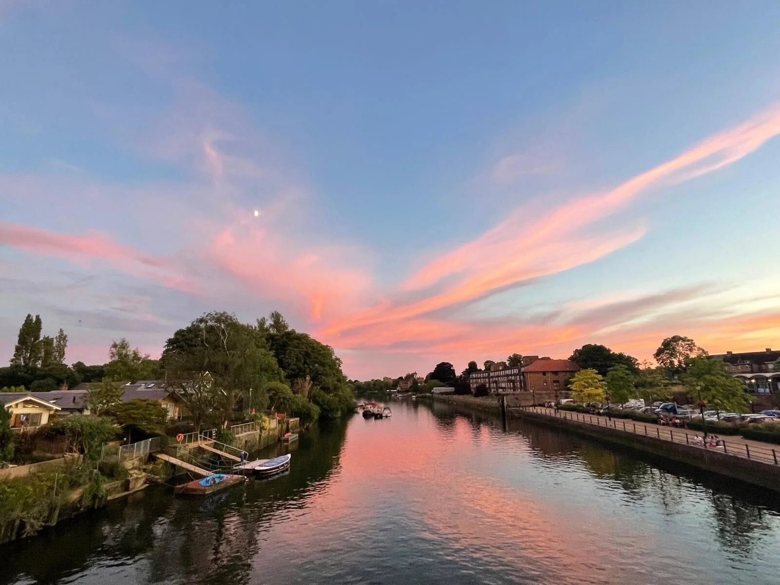 Sunset over a river with colourful clouds in the sky and residential buildings and trees along the water's edge.