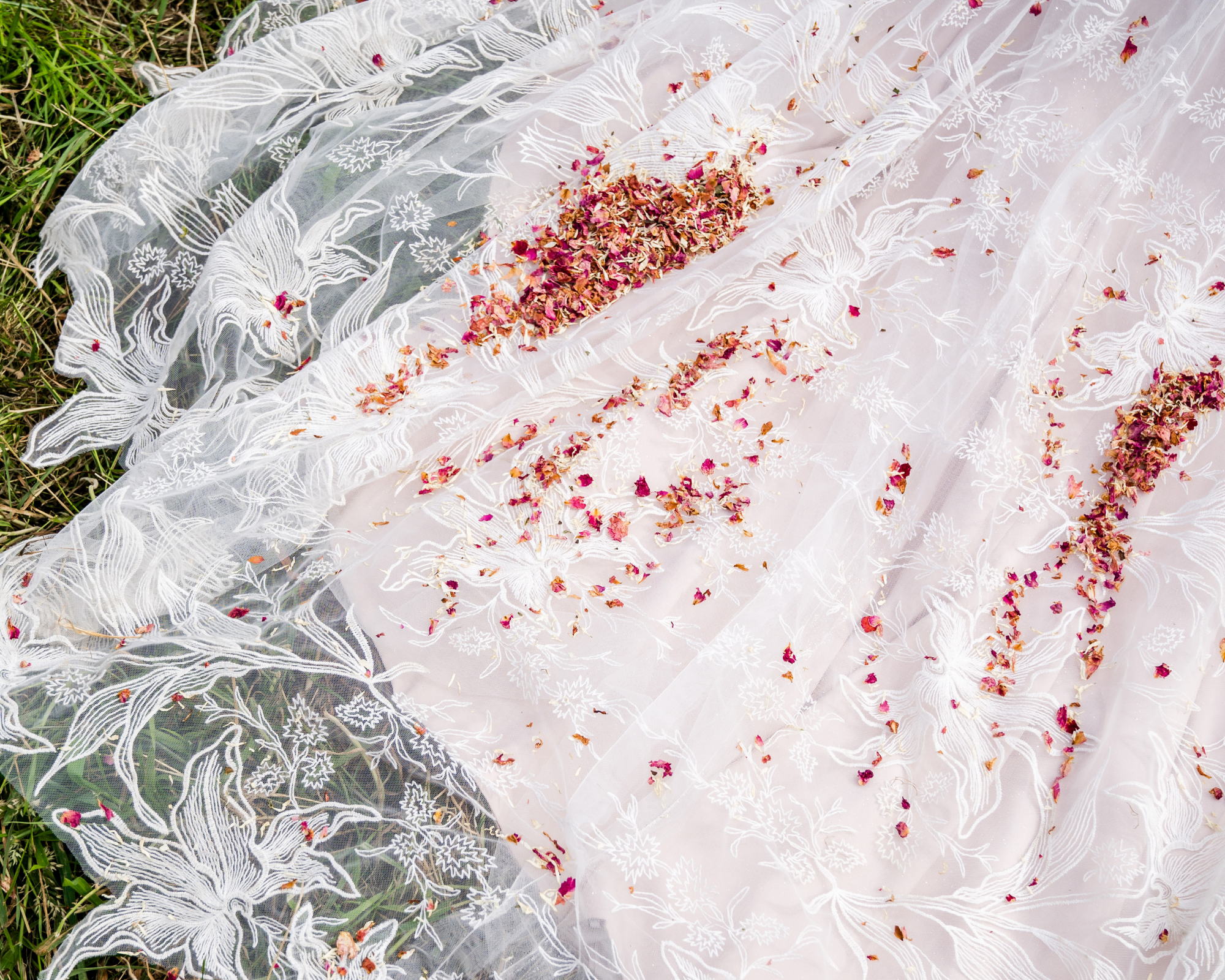 Trouwkleed bedekt met gedroogde rozenblaadjes, gelegen op gras.