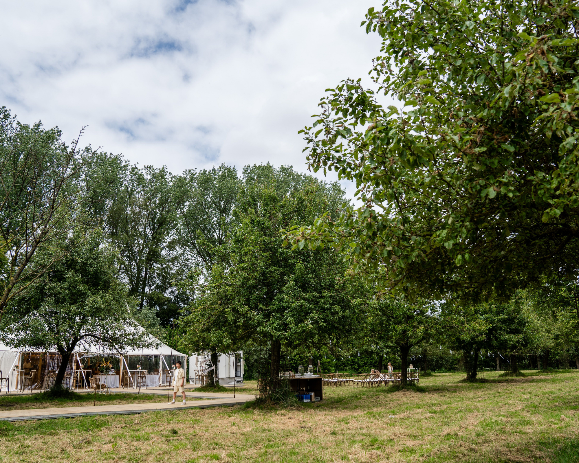 Tent op een grasveld met rondom groene bomen en een bewolkte blauwe lucht.