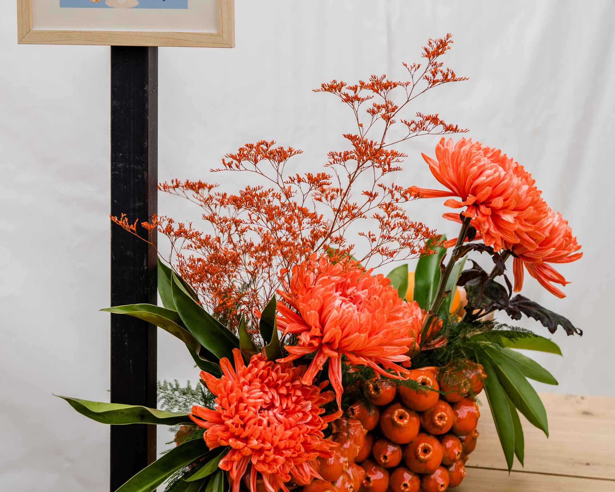 Een bloemenarrangement met grote oranje bloemen, groene bladeren en kleine oranje vruchten in een mand op een houten tafel. Decoratie voor een feest of huwelijk.