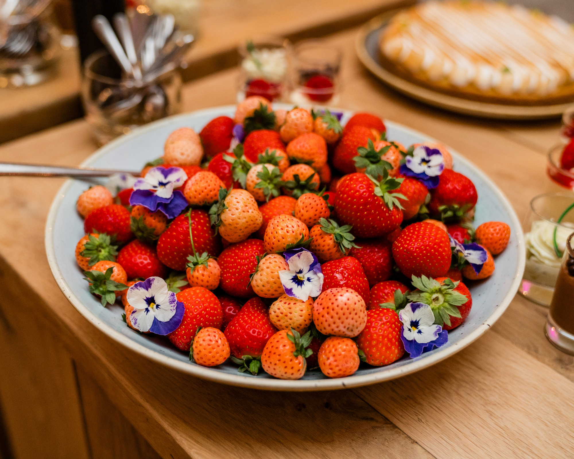 Mand met verse aardbeien en paarse bloemen op tafel.