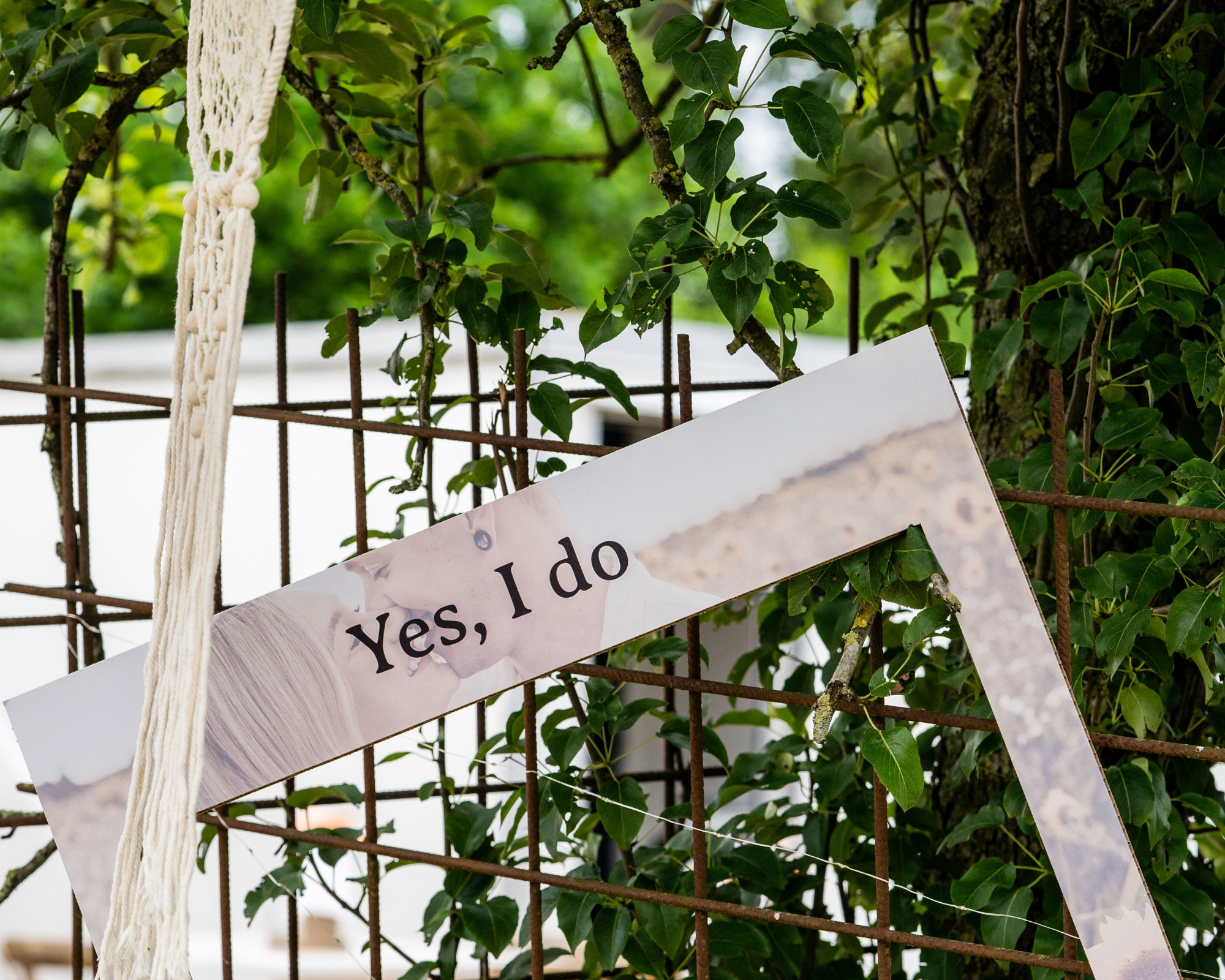 Een muur van sierlijk ijzerdraad en groene bladeren met een bord waarop staat 'Yes, I do', bevestigd aan de ijzerdraad.