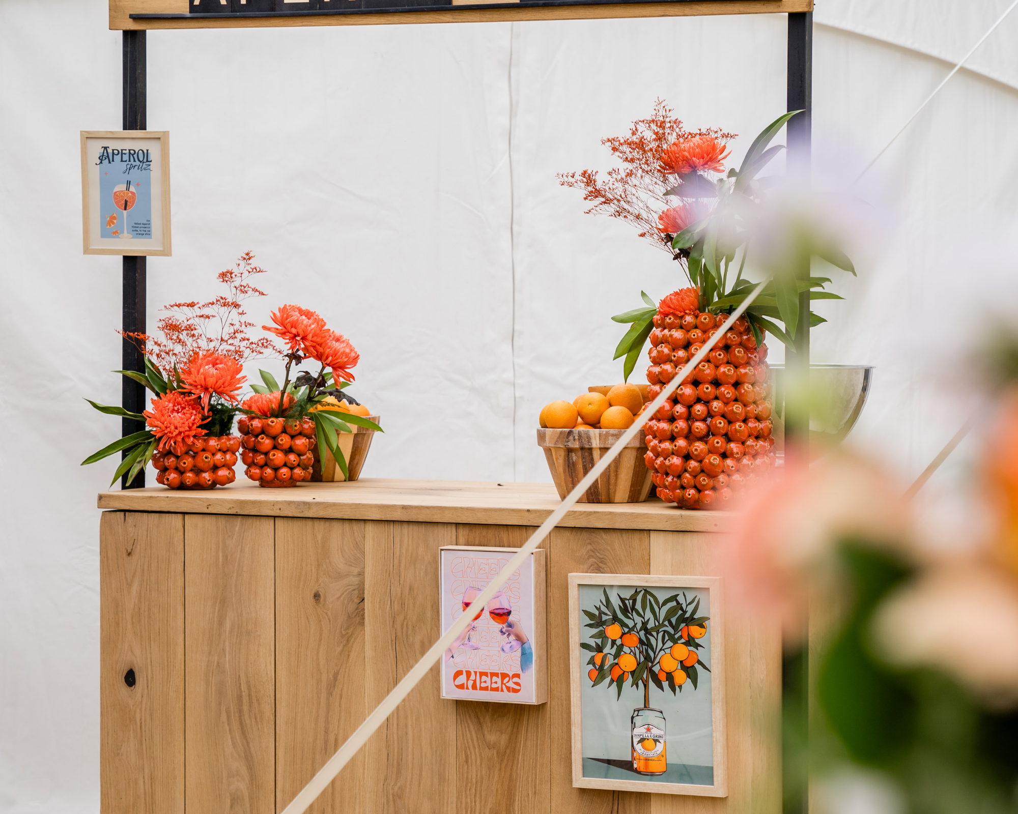 Een houten tafel met vazen gevuld met oranje bloemen en fruit, waaronder appels en citrusvruchten, decoratie. Bar op een huwelijksfeest.