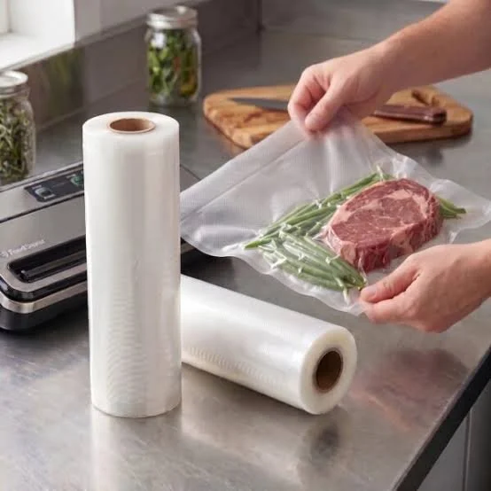 Une main qui emballe de la viande dans un sac de cuisson sous vide, avec un rouleau de film plastique à côté.