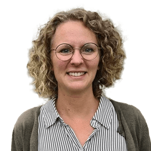 En kvinna med lockigt hår, glasögon och en randig skjorta, som ler.