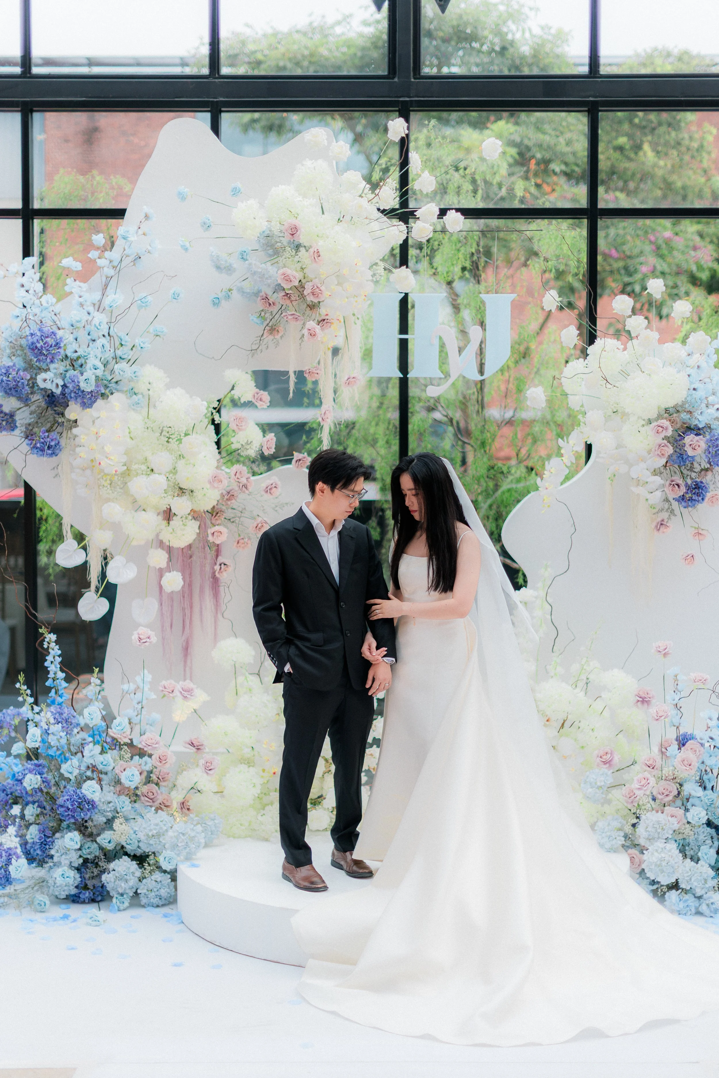 A bride and groom standing together on a wedding stage with floral decorations and the words "I do" in the background.