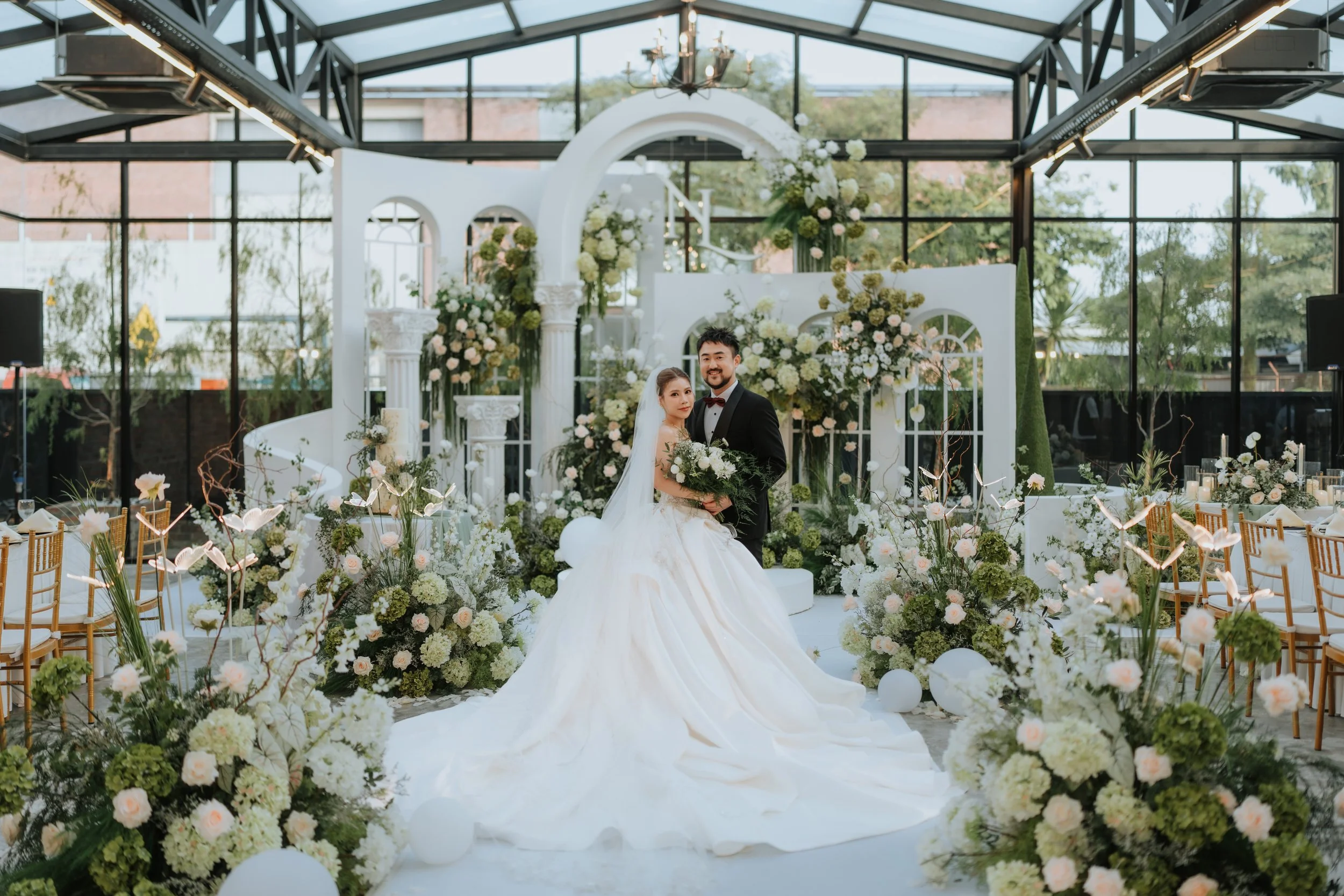 Bride and groom posing together at a wedding ceremony with a floral and white decor background.