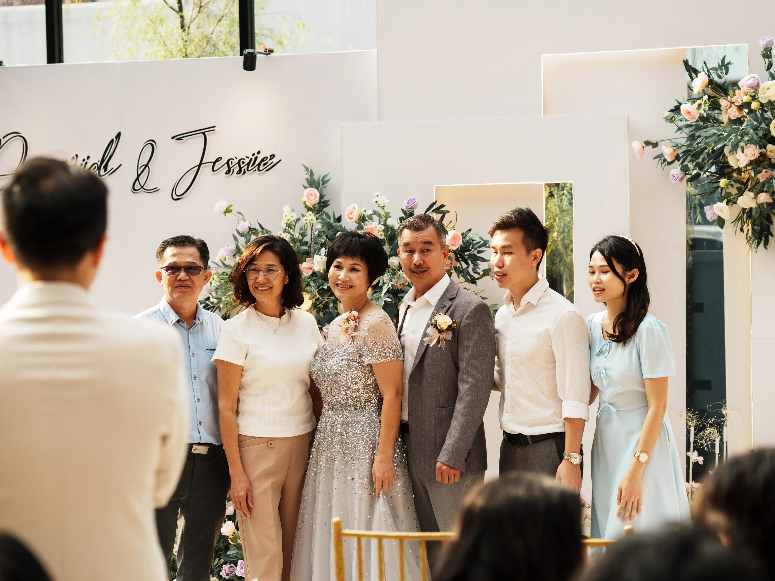 A bride and groom standing with four family members in front of a decorated backdrop at a wedding celebration.
