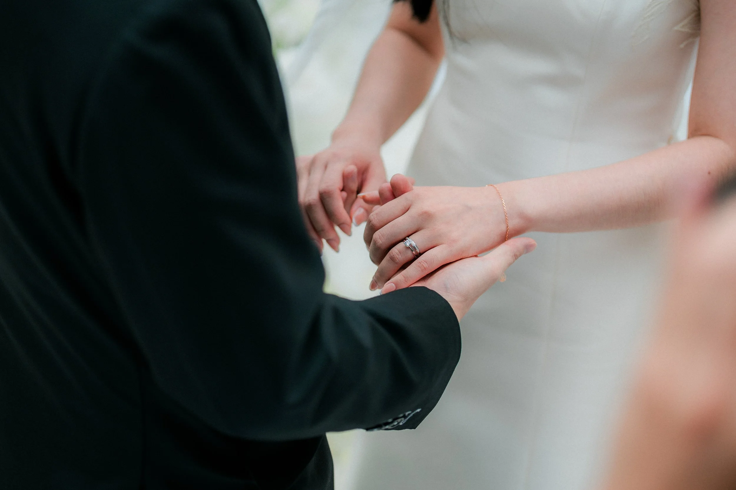 A wedding ceremony with a bride and groom holding hands, showing the bride's engagement ring and wedding band.