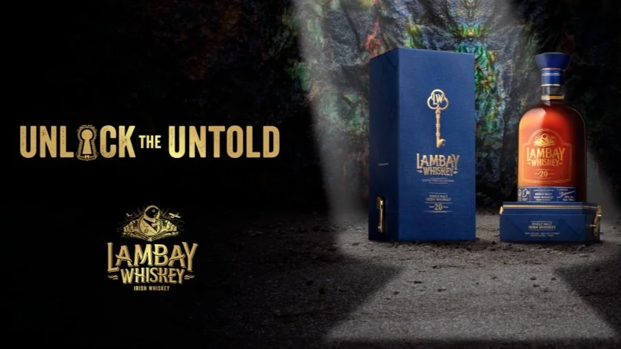 Lambay Irish Whiskey bottle and box with the text 'Unlock the Untold' and the Lambay Whiskey logo on a rugged outdoor background.