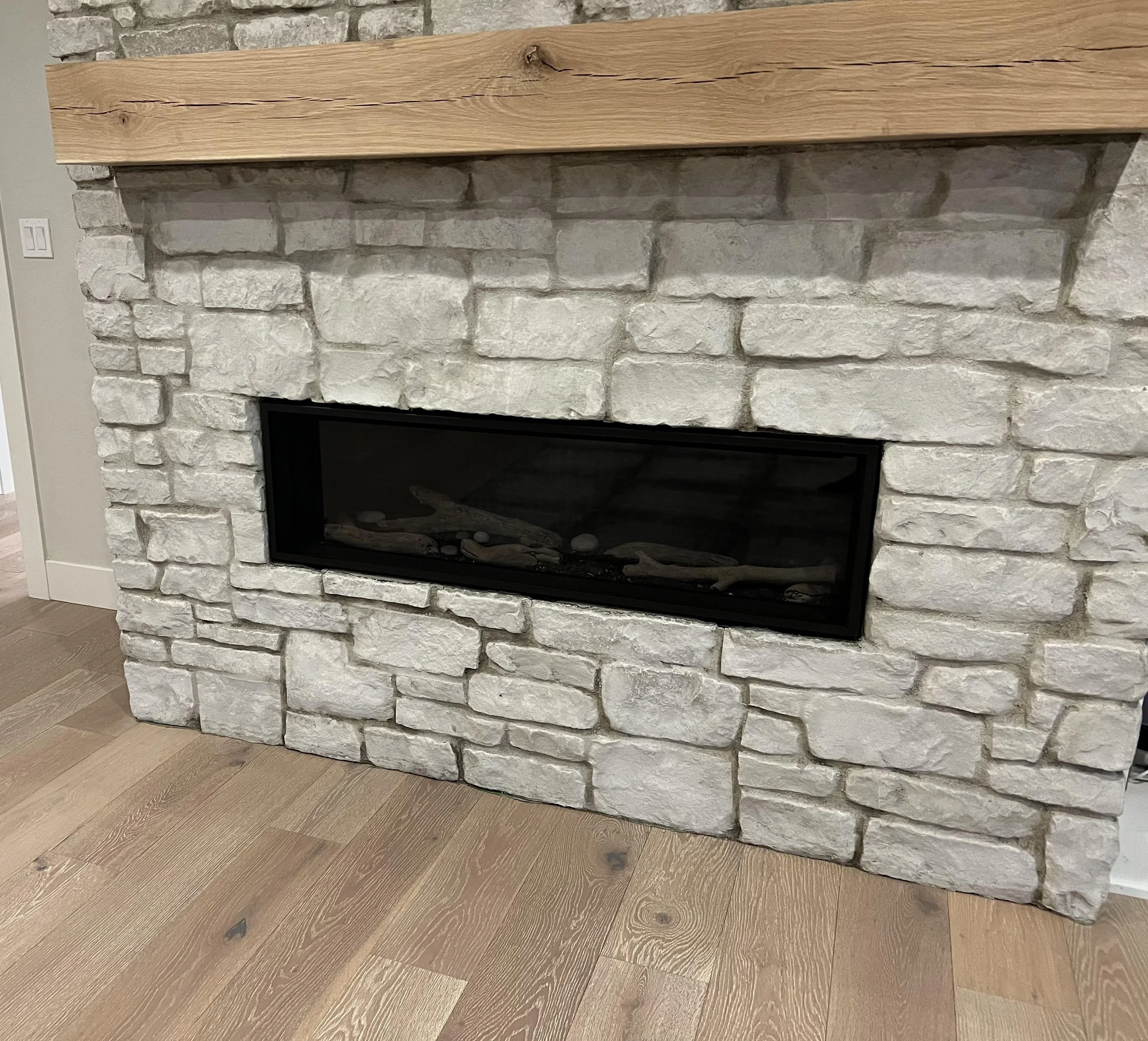A close-up view of a modern white brick fireplace with a wooden mantel and a black glass opening, placed on a hardwood floor.
