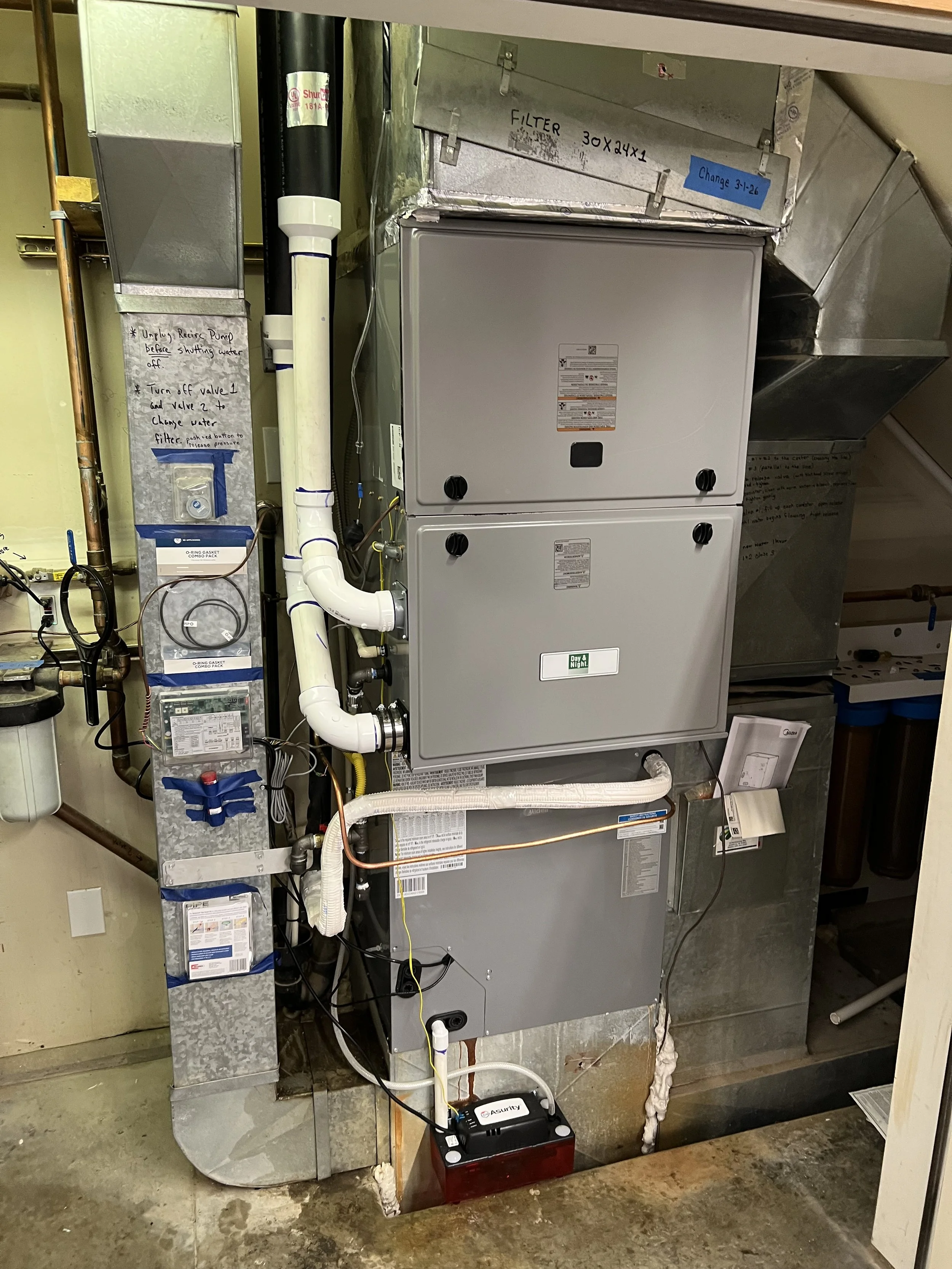 View of an HVAC or water heater system with various pipes, valves, and electrical connections in a utility room.