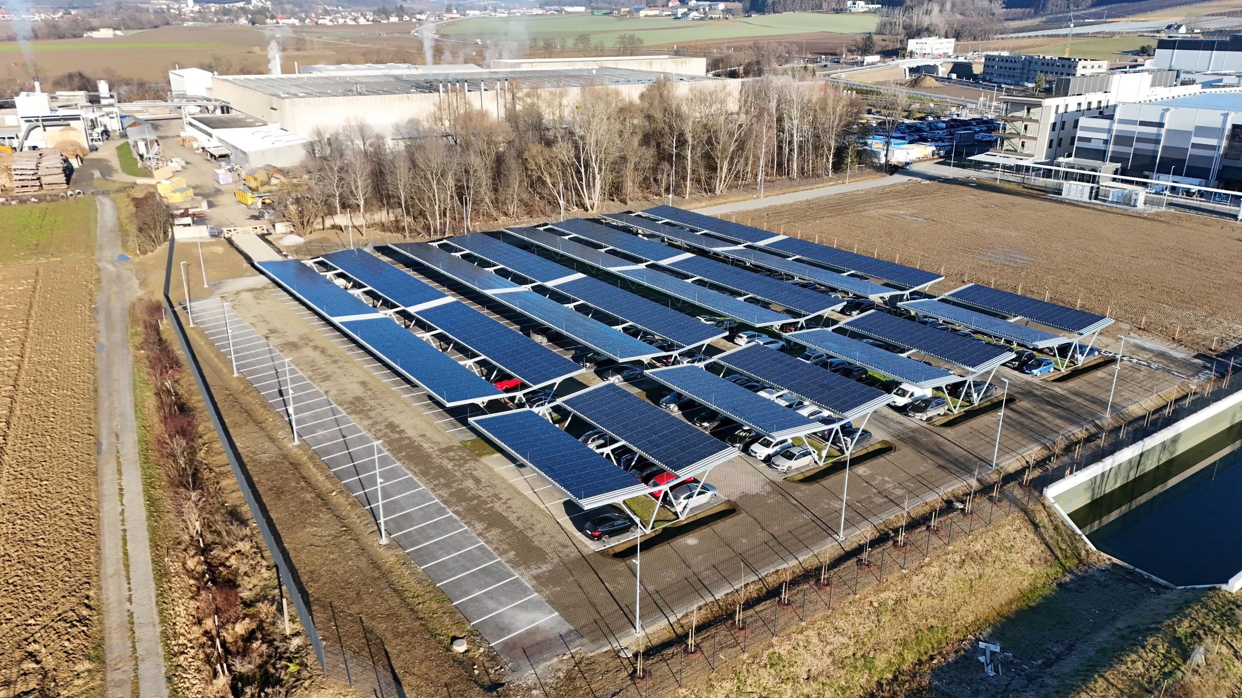 PV-Carport-Anlage in Wollsdorf mit Stahlkonstruktion und integrierten Photovoltaikmodulen über einem Parkplatz zur Stromerzeugung und Fahrzeugüberdachung.