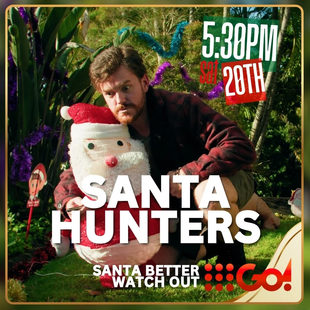 A man with brown hair and beard crouching next to a Santa Claus plush toy. The background features green foliage and colorful decorations. The overlay text indicates the date and time as Saturday at 5:30 PM on the 20th, with the event titled "Santa Hunters" and a warning to "Santa Better Watch Out".