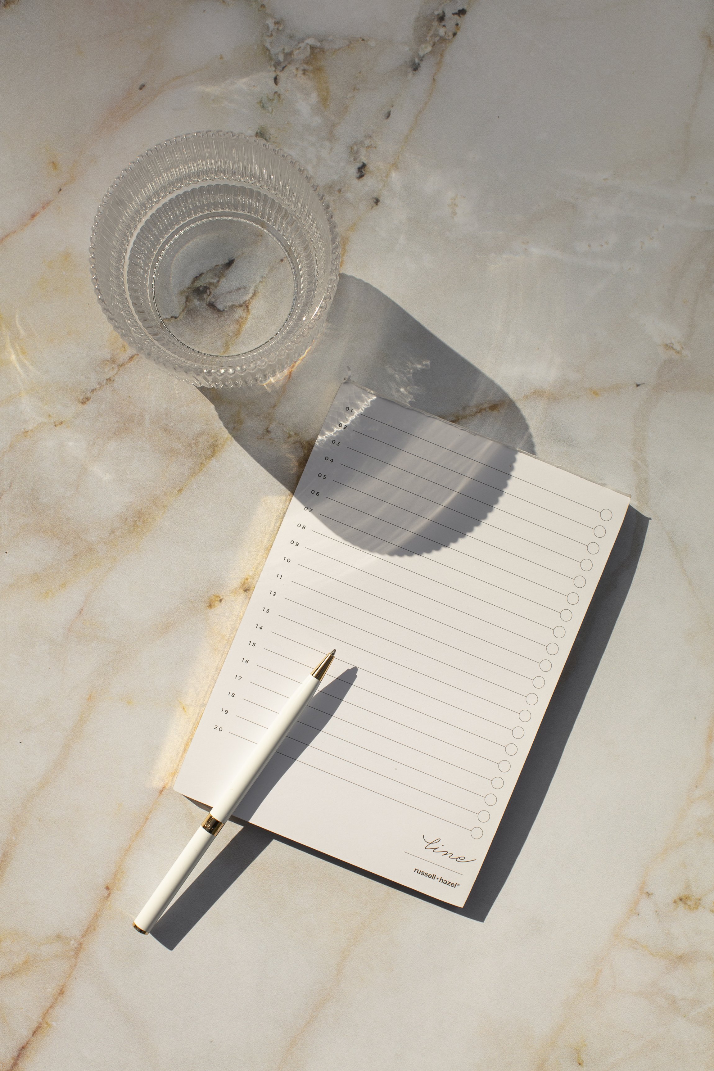 glass next to a notepad with pen on top