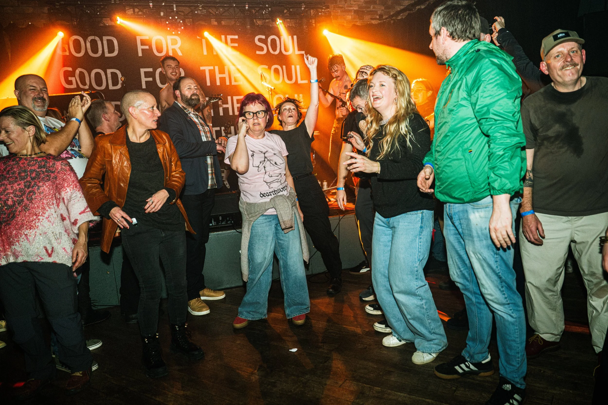 People dancing and having fun at a concert or party with orange stage lights and a backdrop with the words "Food for the Soul"