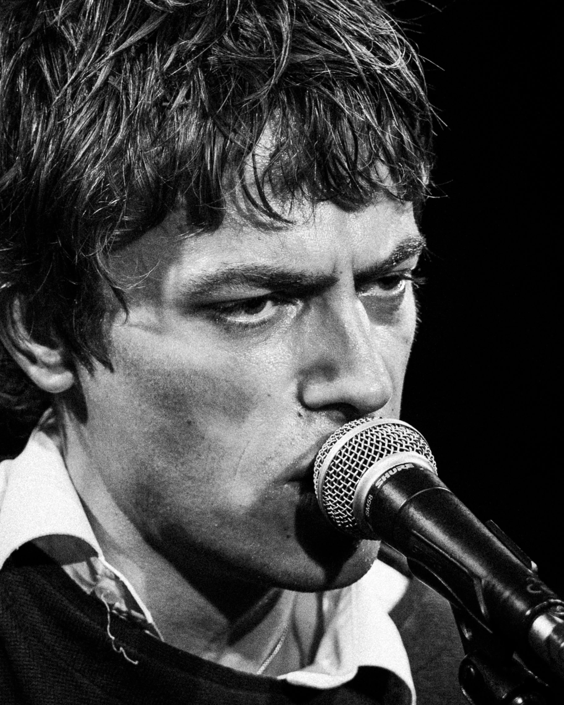 Close-up black and white photo of a man singing or speaking into a microphone.