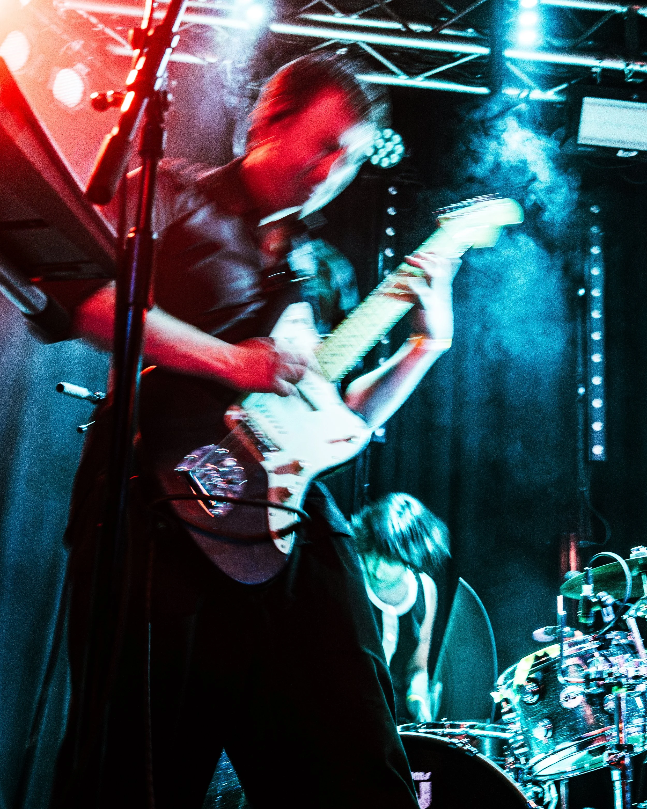 Musician playing electric guitar on stage with colorful lights and smoke effects.