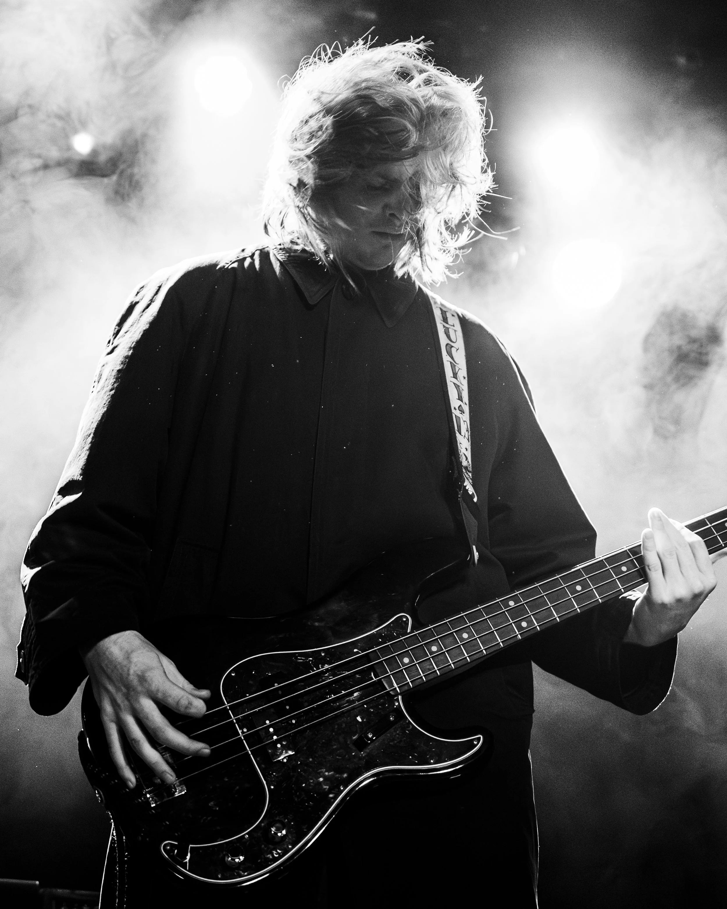 A person playing an electric bass guitar on stage with bright stage lights behind them.
