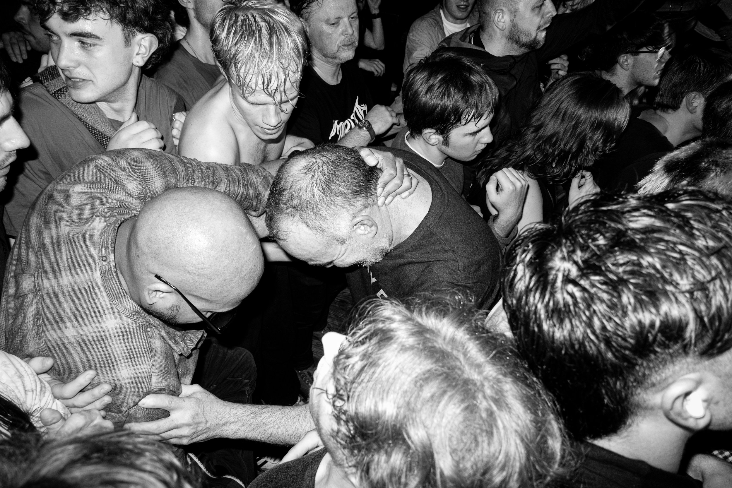 Crowd of people at a concert or event, some with hands raised, one person holding their head, others looking in various directions, black and white photo.