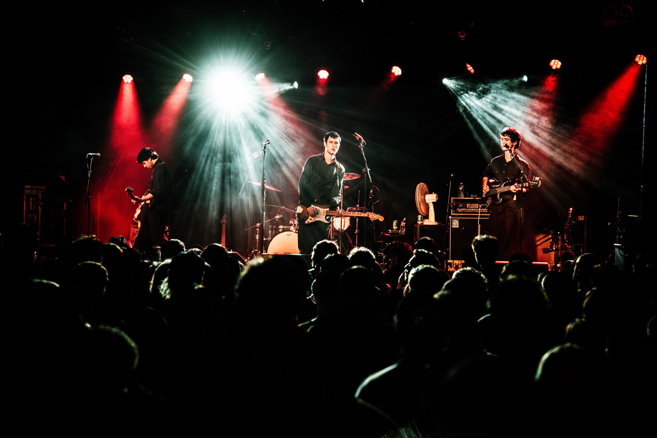 A band performs on stage in front of an audience, with colorful stage lights and musical instruments.