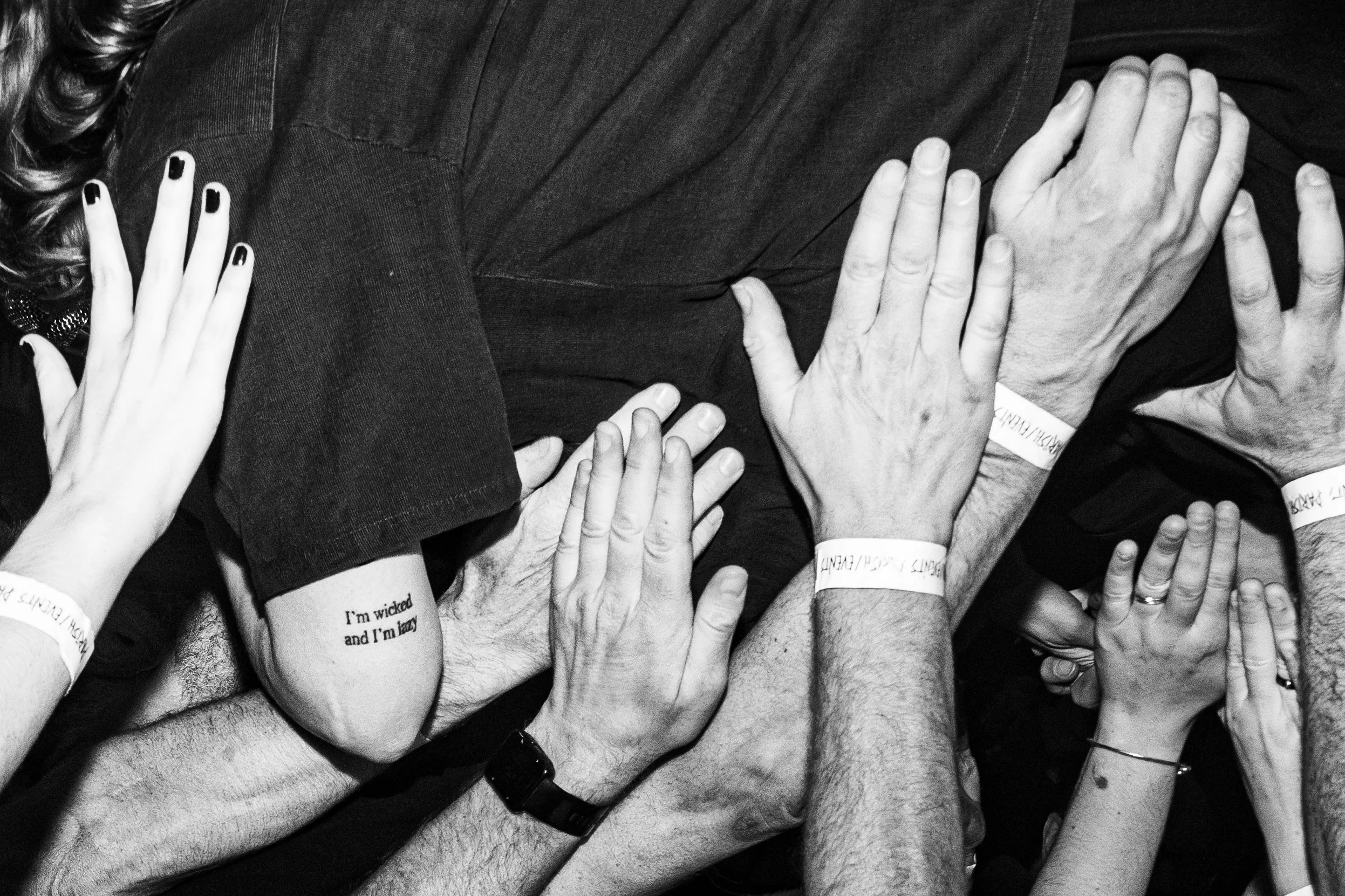 Multiple hands of different sizes and skin tones reaching out and holding a person's body, some with wristbands.