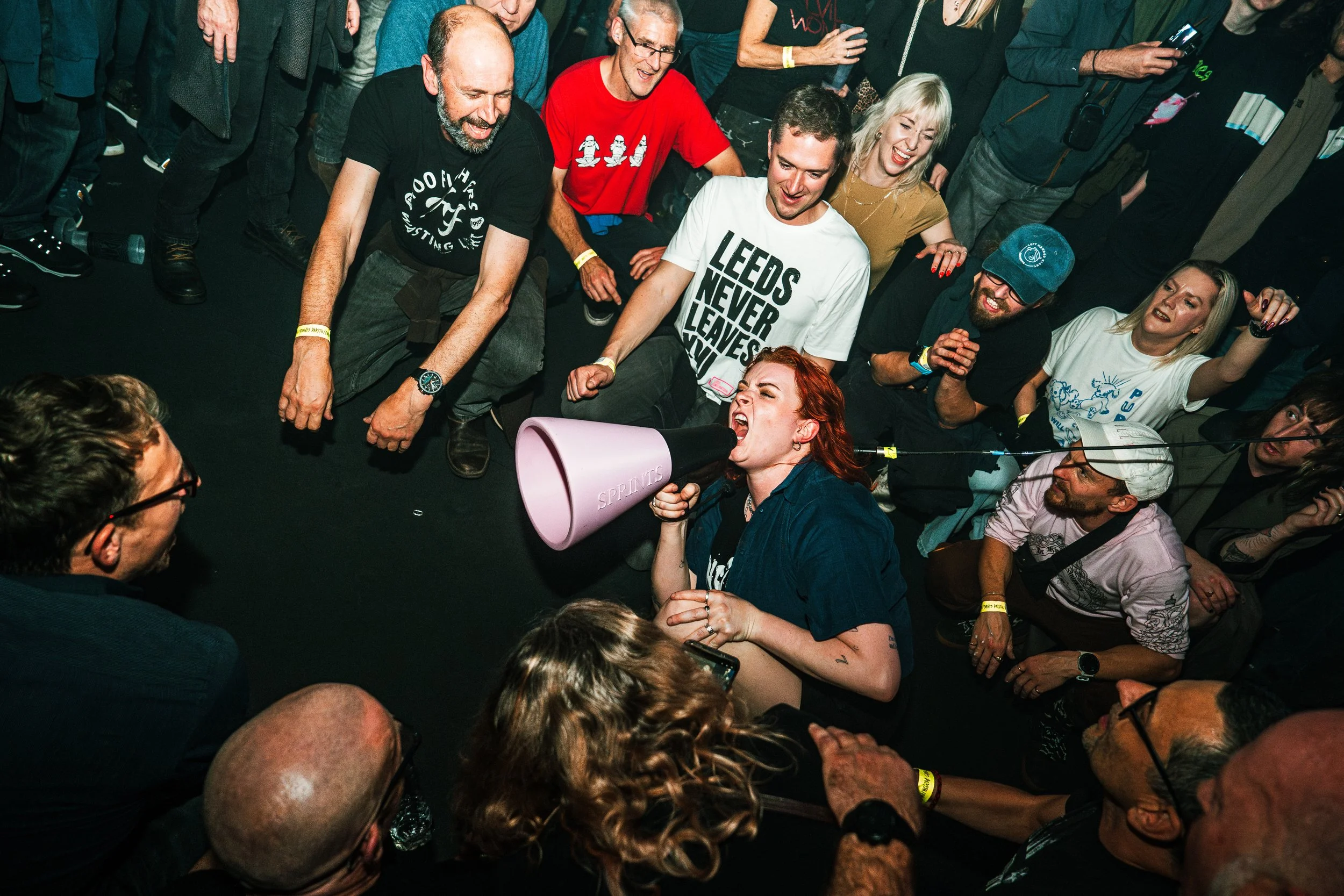 A woman with red hair is screaming into a megaphone at a crowded event, surrounded by people who are watching and laughing.