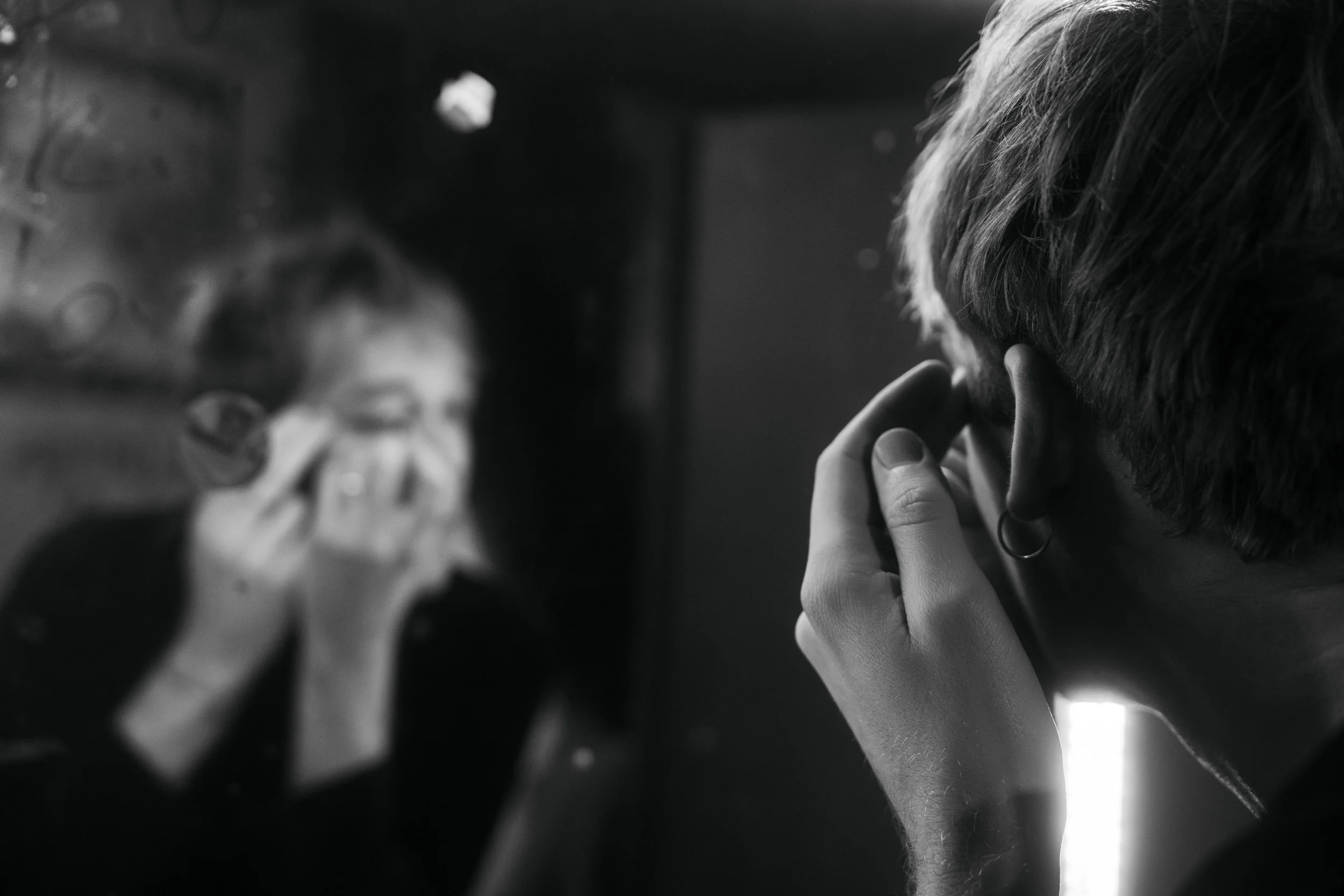 A woman looking in a mirror adjusting her makeup with her fingers, with her reflection visible.