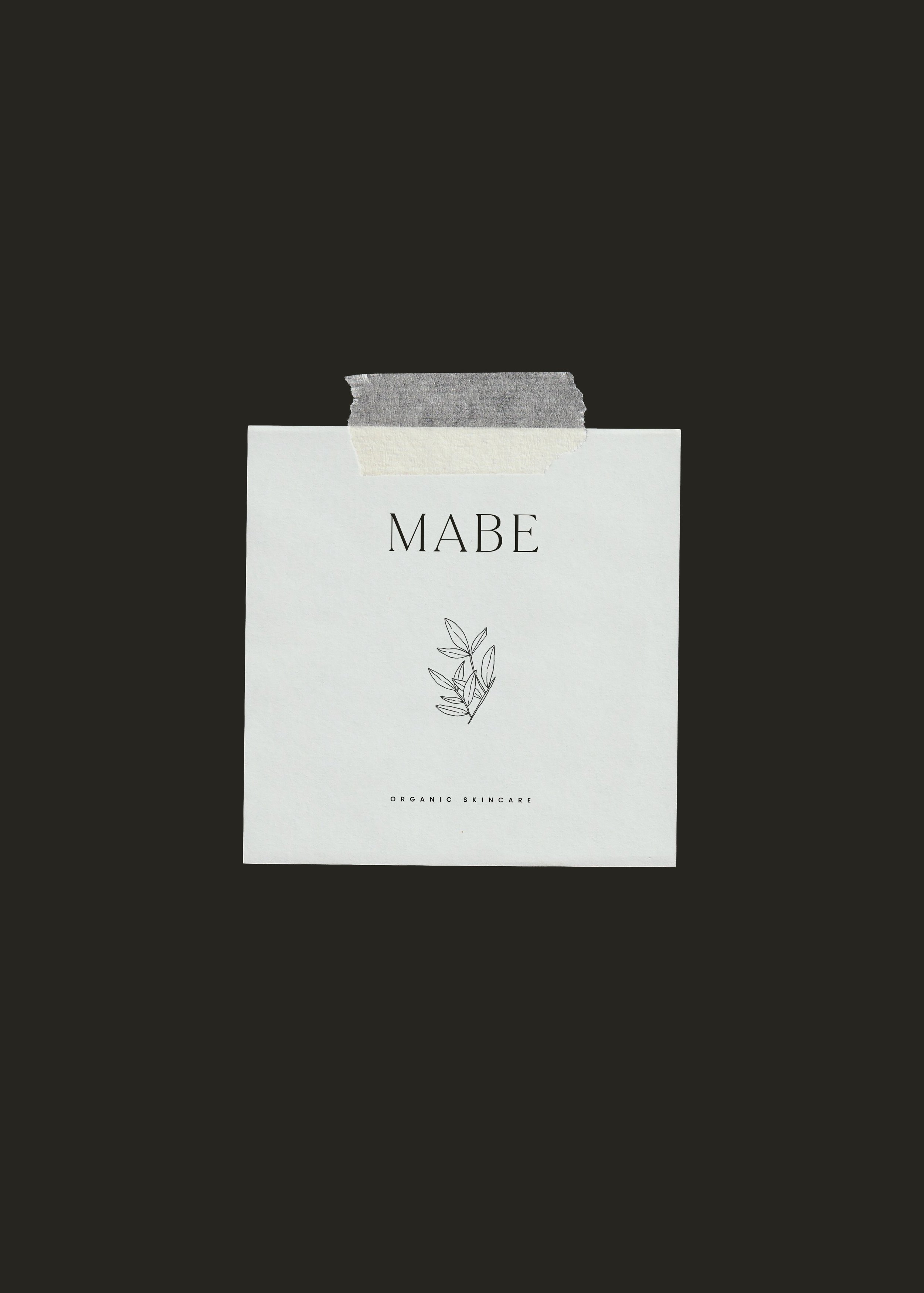 Mäbe organic skincare brand identity featuring a minimalist logo and botanical illustration on a white card taped against a dark textured background.