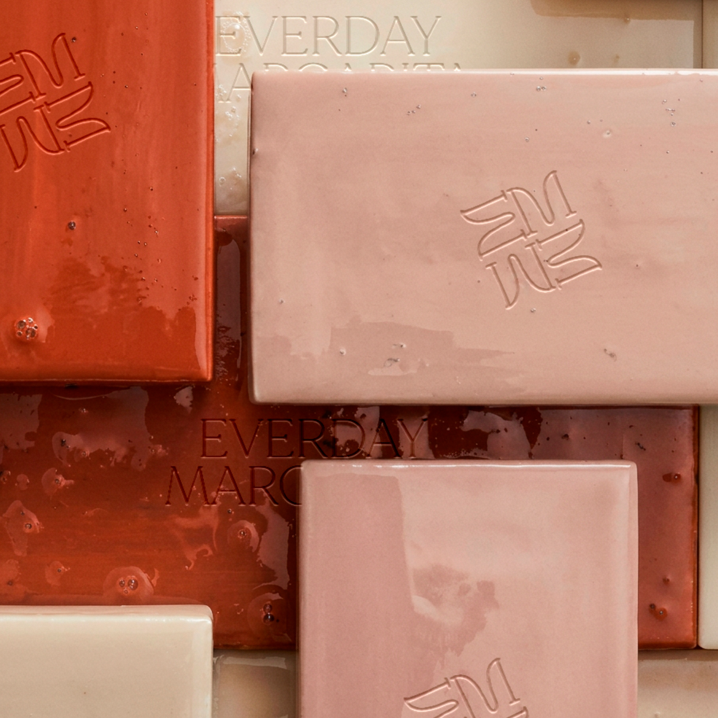 A close-up view of several soap bars in shades of pink, red, and white, with the words 'EVERYDAY' and 'MARC' embossed on some of them, arranged closely together.