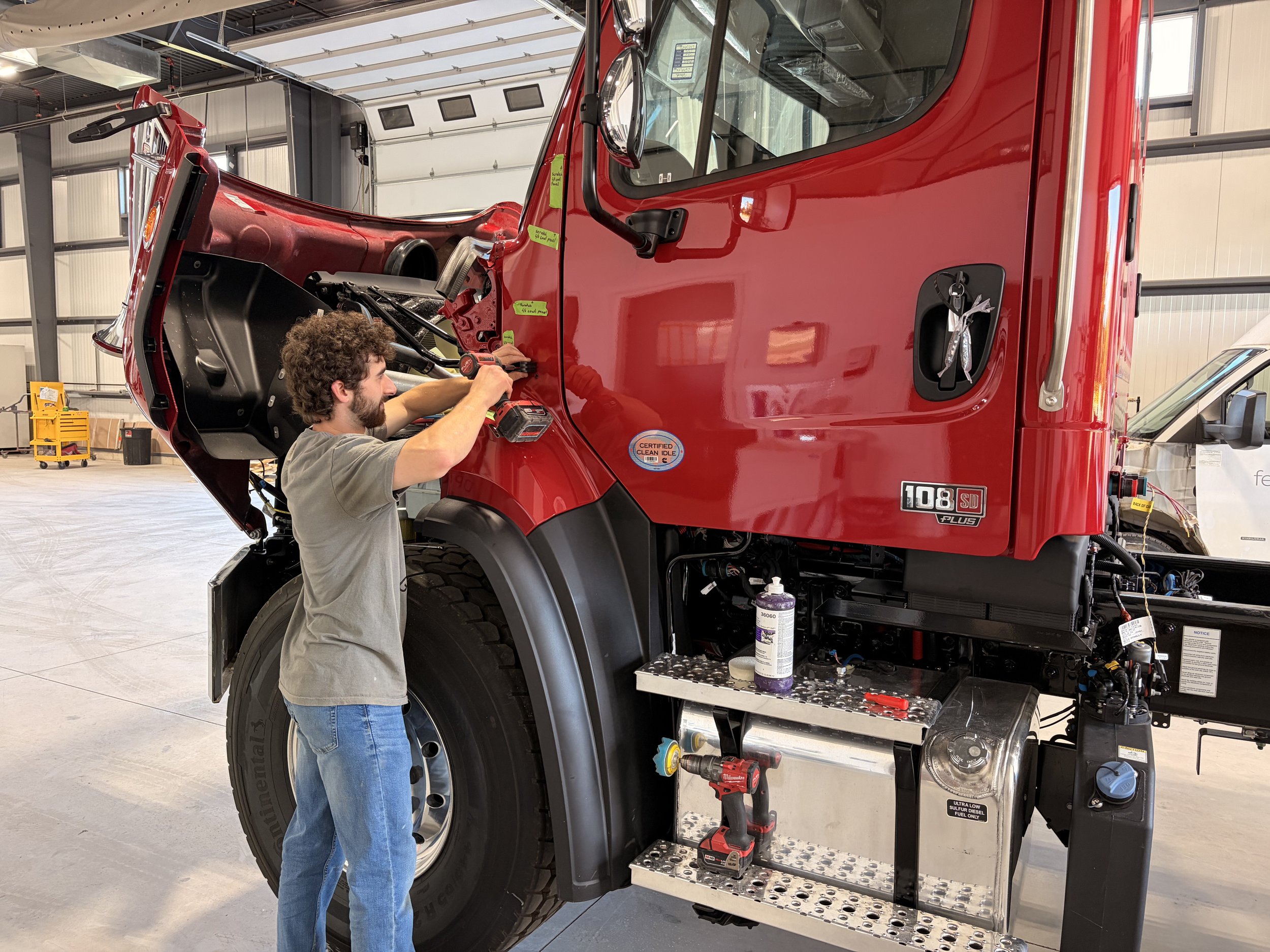 Body shop tech working on a large red fire truck at Optimus Body Shop. Truck wash, trailer washout, diesel repair, propane autogas, fleet maintenance, Walker MI