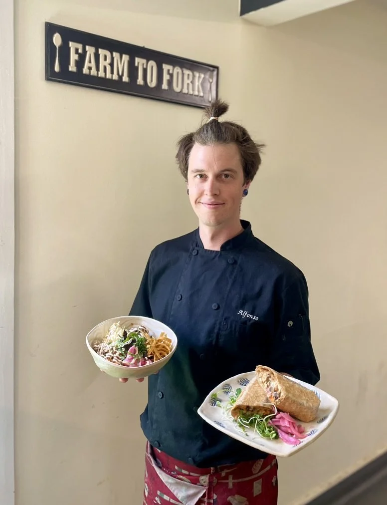 a chef displays two fresh plates of food in front of a farm to fork sign.
