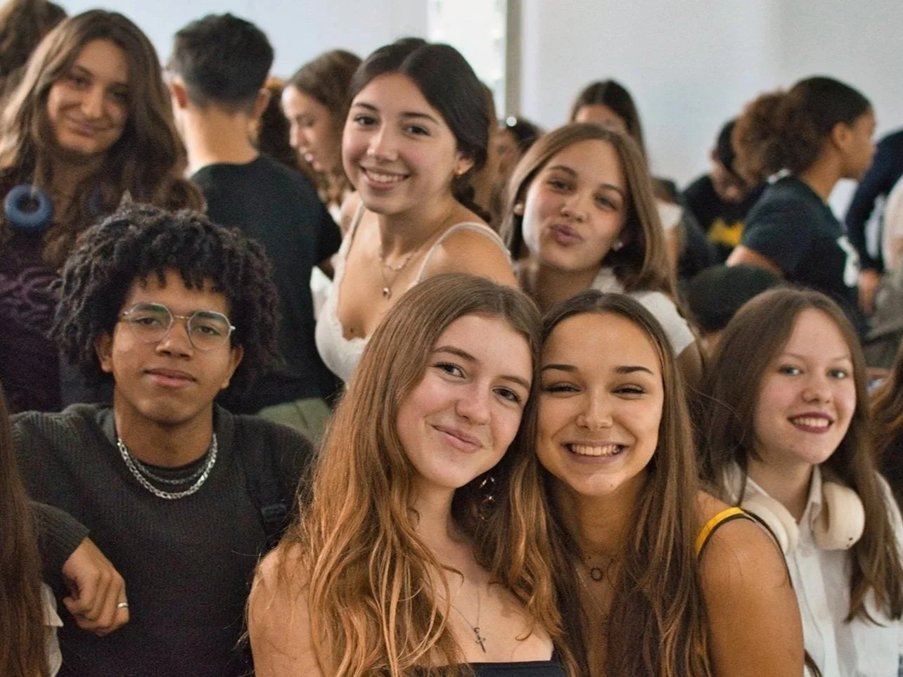 Group of teenagers smiling and posing for a photo at an indoor gathering.
