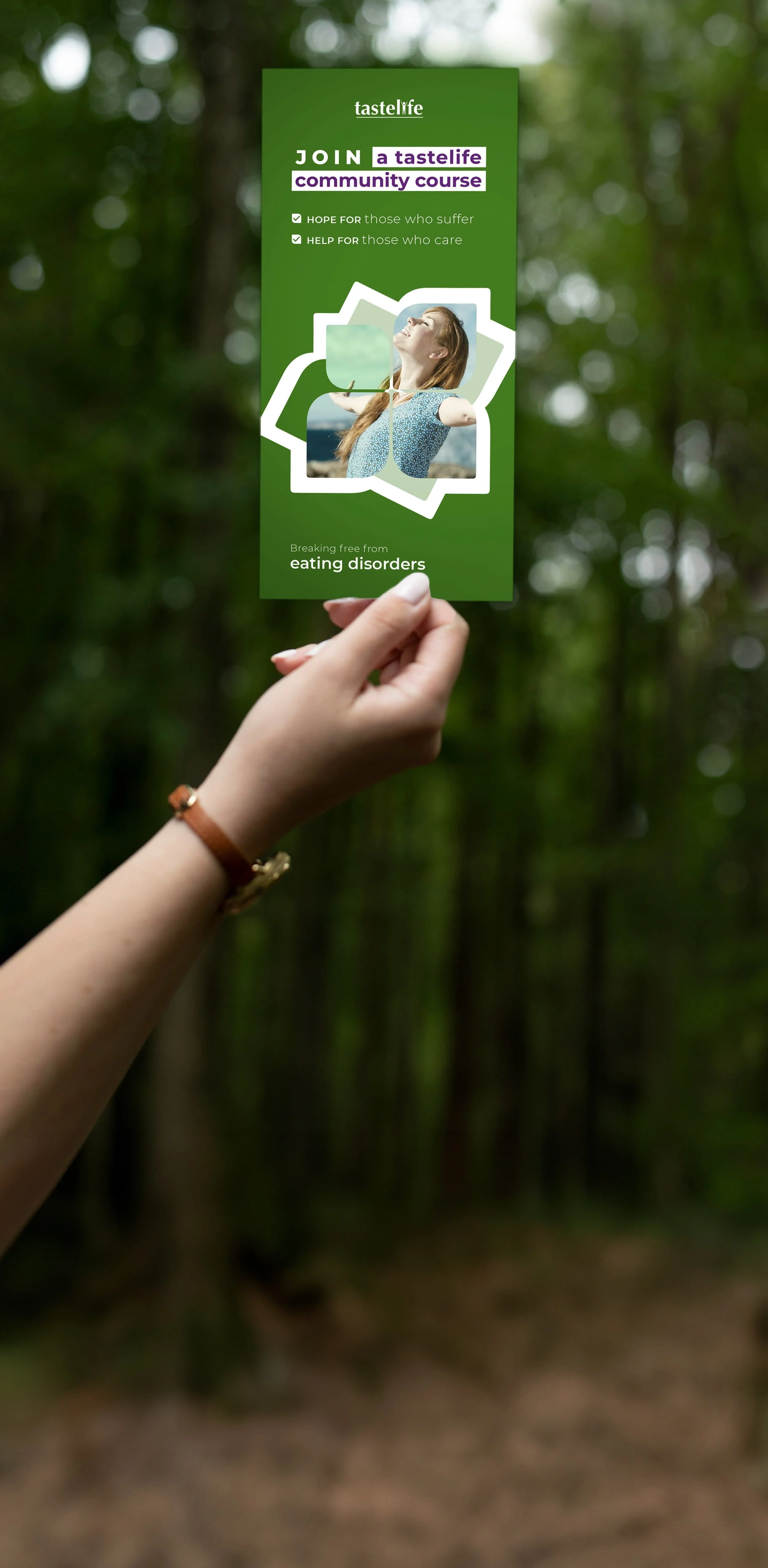 A hand holding a green brochure titled 'Join a Tastelife Community Course,' with a smiling woman on the cover, set against a blurred forest background.