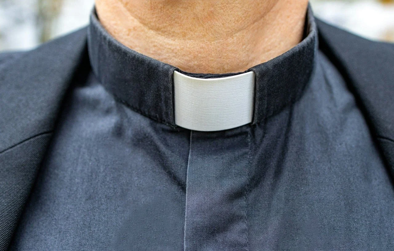 Close-up of a person wearing a black clerical shirt with a white clerical collar, commonly worn by clergy.